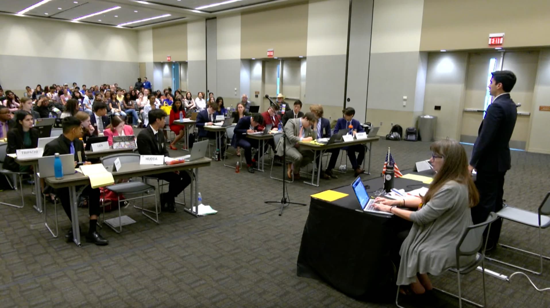 A group of students in a room, large desks are in a row.